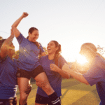 Women football team celebrating winning soccer match lifting player