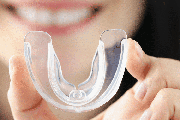 Smiling Woman Holds Transparent Plastic Mouth Guard in Her Hand