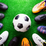 Top view of a soccer ball and various cleats on green ground