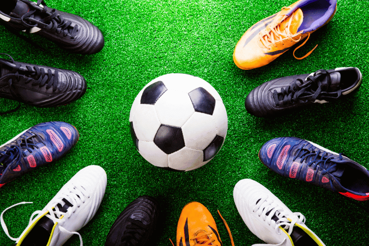 Top view of a soccer ball and various cleats on green playground