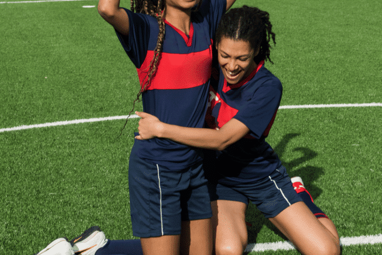 Two female football players celebrating their win doing knee sliding